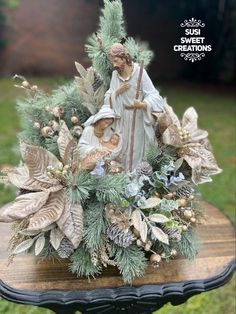 a statue of the virgin mary and child jesus surrounded by greenery on a table