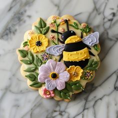 a decorated cookie with flowers and a bee on it's side sitting on a marble surface