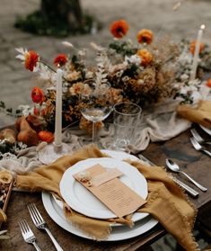 the table is set with white plates, silverware and orange floral centerpieces