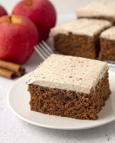 a piece of carrot cake on a plate with cinnamon sticks and apples in the background