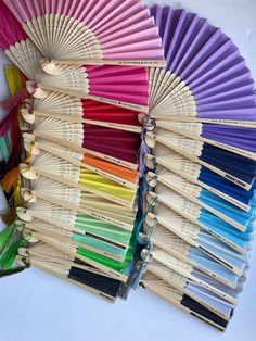 many different colors of paper fan sitting next to each other on a white table top