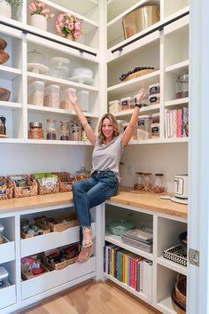 a woman sitting on top of a wooden shelf in a kitchen filled with lots of shelves