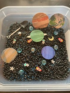 a plastic container filled with lots of different planets on top of black rocks and gravel