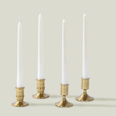 three white candles are lined up next to each other in gold holders on a gray background