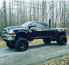 a large black truck parked on the side of a road in front of some trees