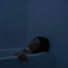 a woman leaning on the edge of a bathtub in the dark with her hand resting on the edge of the tub