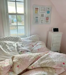 an unmade bed in a bedroom with pink walls and pictures on the window sill