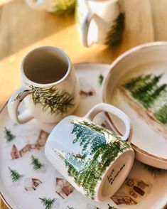 two cups and saucers with trees on them sitting on a table next to each other