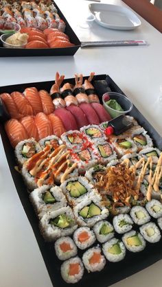 two trays filled with different types of sushi on top of a white table