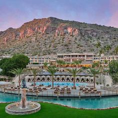 an outdoor swimming pool surrounded by palm trees and mountains in front of a resort building