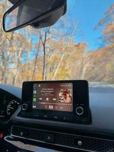 the dashboard of a car with an electronic device on it's dash board and trees in the background