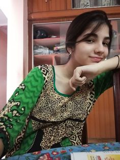 a woman sitting on top of a bed next to a book shelf with a green shirt