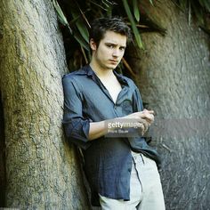 a young man leaning against a tree with his arms crossed