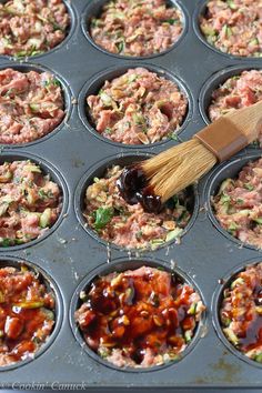 a muffin tin filled with cupcakes covered in toppings and a wooden spatula