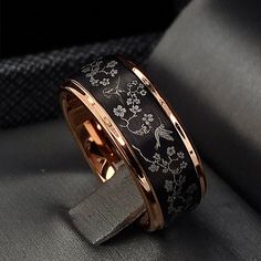 a black and gold wedding ring with flowers on the inside is sitting on a gray surface