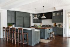 a large kitchen with gray cabinets and wooden flooring is pictured in this image, there are stools at the center of the island