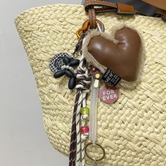 a straw bag with various items hanging from it's handles and straps, including a heart shaped keychain