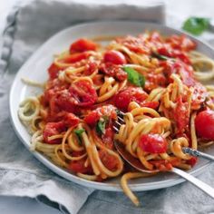 a plate of spaghetti with tomatoes and basil on the side, ready to be eaten