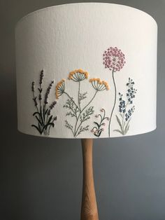 a lamp with flowers painted on it sitting on top of a wooden table next to a gray wall