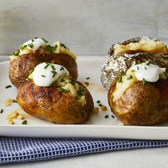 three baked potatoes on a white plate topped with sour cream