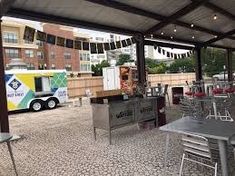 an outdoor dining area with tables and chairs under a covered patio next to a food truck