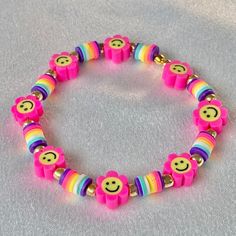 a pink bracelet with smiley face beads and rainbows on the bead is sitting on a gray surface