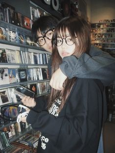 two people standing next to each other in front of a wall full of cds and dvds