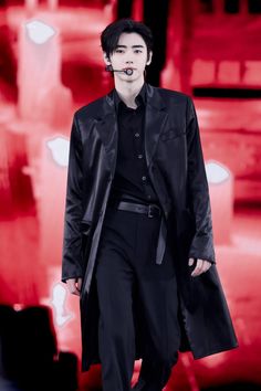 a male in a black suit and tie is walking down the runway with his mouth open