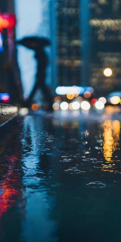 people walking down the street at night with umbrellas in the rain and cars on the road