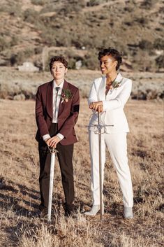 two men in suits standing next to each other with swords on their hands and one holding a flower