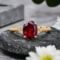 a red stone ring sitting on top of a rock next to daisies and flowers