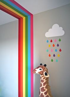 a giraffe standing in front of a rainbow painted wall with clouds and rain drops