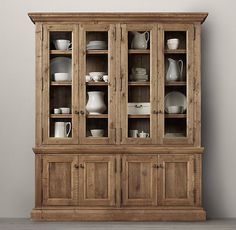 an old wooden china cabinet with glass doors and dishes on it's shelves, against a brown wall