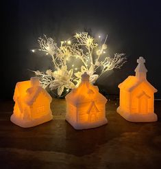 three small houses are lit up in the dark with christmas lights behind them and a tree