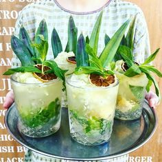 a person holding a tray with three glasses filled with ice and mint sprigs