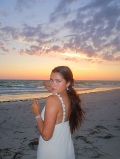 a beautiful young woman standing on top of a beach next to the ocean at sunset