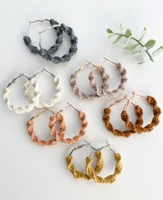 six pairs of hoop earrings with braided ends on a white surface next to a plant