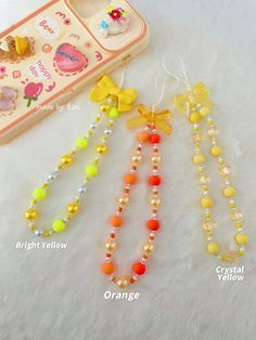 three necklaces with bows and beads on top of a white surface next to a cell phone