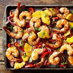 shrimp and pineapple stir fry on a baking sheet with onions, peppers, and lemon wedges