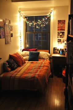 a bed sitting in a bedroom next to a window with christmas lights on the windowsill