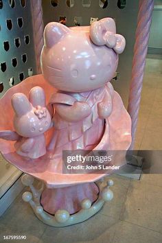 a hello kitty statue sitting on top of a pink saucer with two small pigs in it