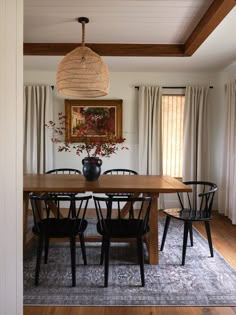 a dining room table with four chairs and a vase on top of it in front of a window