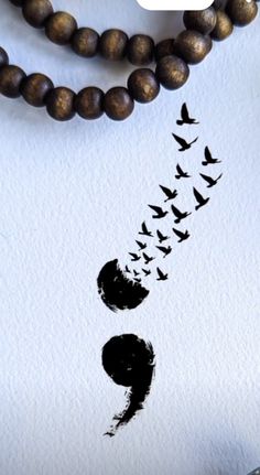 a necklace with birds flying over it on top of a white table next to a wooden bead necklace