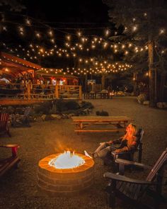 a woman sitting in front of a fire pit at night