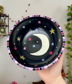 a hand holding a black bowl with stars and a crescent painted on it