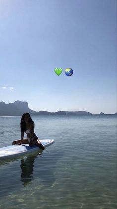 a person on a surfboard in the water with a heart shaped balloon flying above