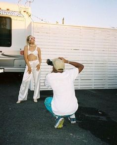 two people are taking pictures in front of a white van and a man is sitting on the ground