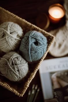 three balls of yarn sit in a basket next to a candle and knitting utensils