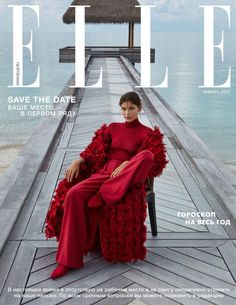 a woman sitting on top of a wooden pier next to the ocean in a red dress