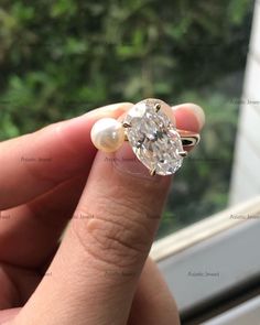 a woman's hand holding an old - fashioned diamond and pearl ring in front of a window